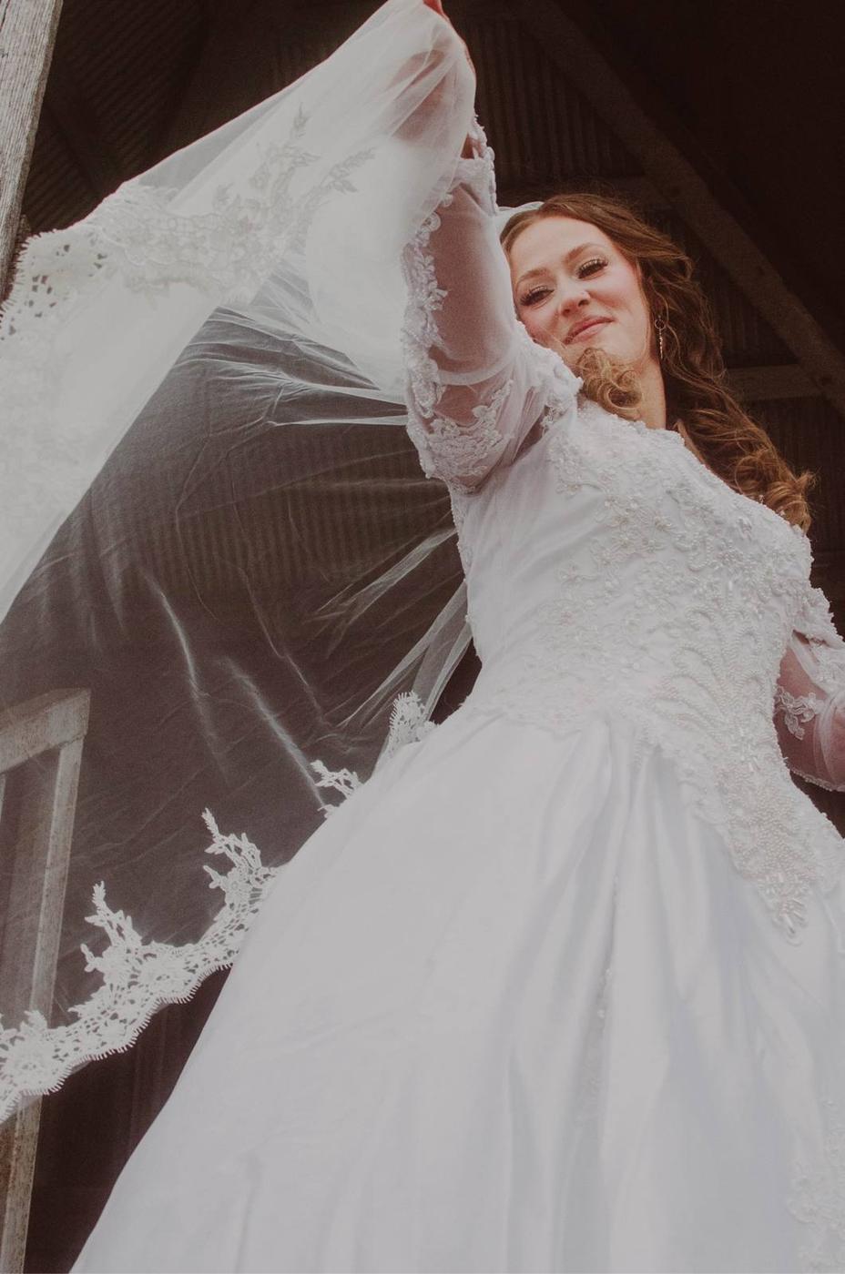 A bride lifting her lace-trimmed veil in a low-angle bridal portrait
