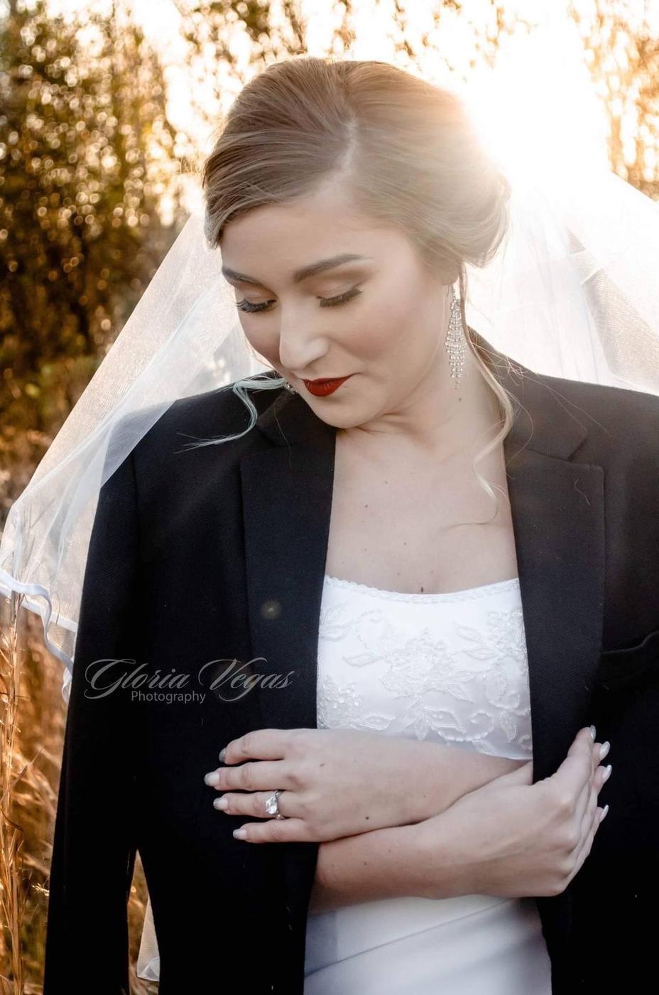 A bride in her veil and a black jacket standing in warm sunlight