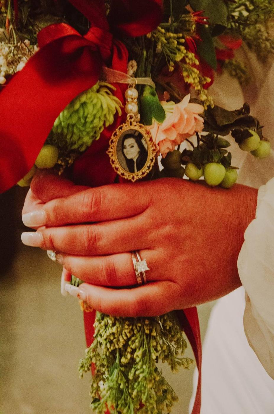 A bride holding a bouquet decorated with a portrait locket and red ribbon