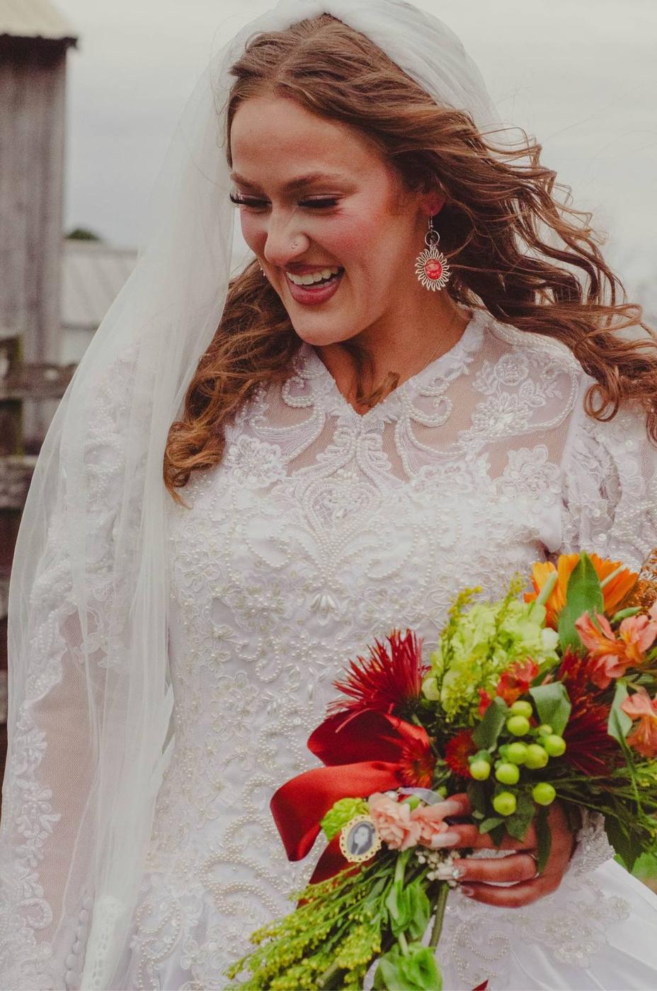 A laughing bride in a lace gown holding a colorful bouquet