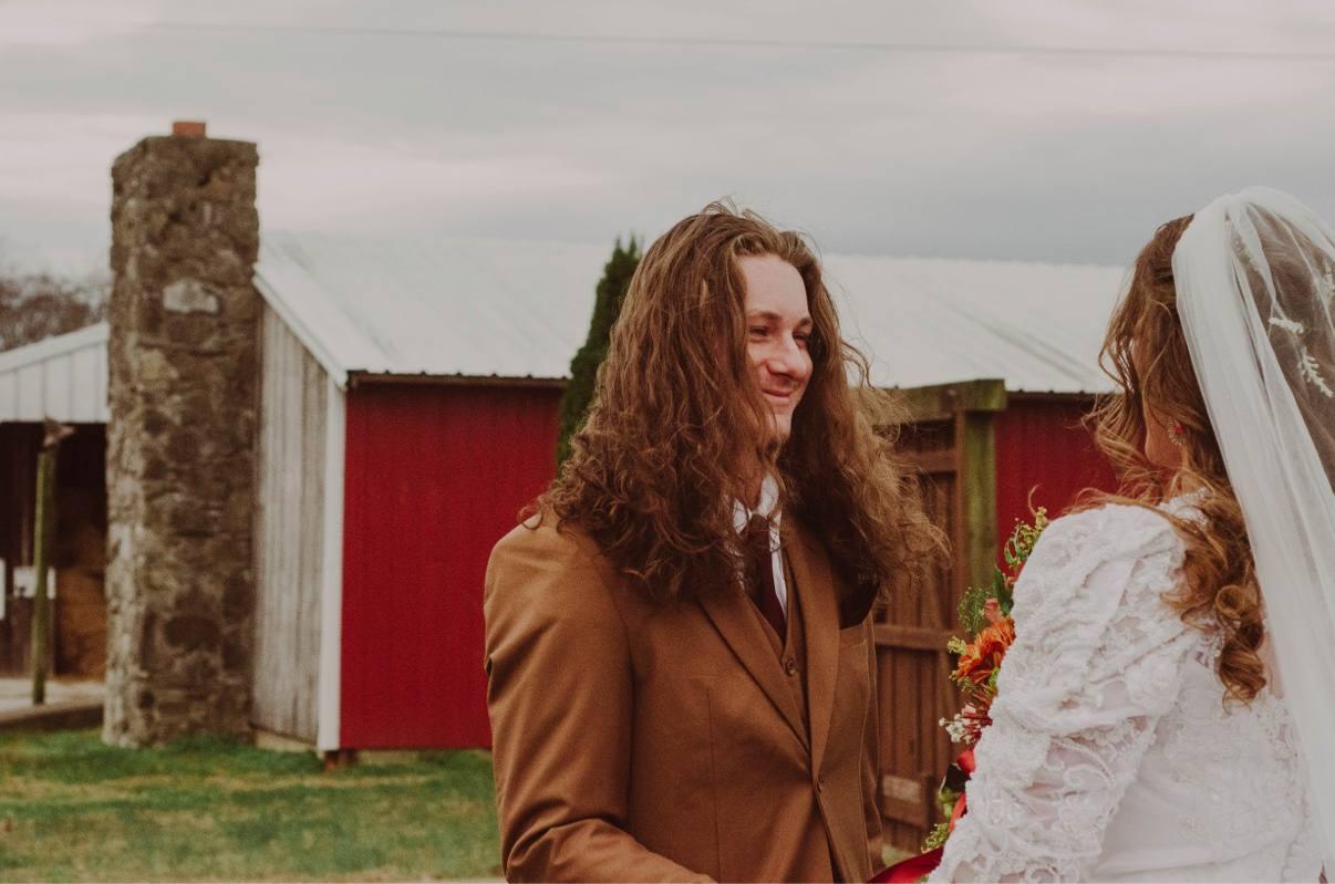 Newlyweds facing each other beside a red barn