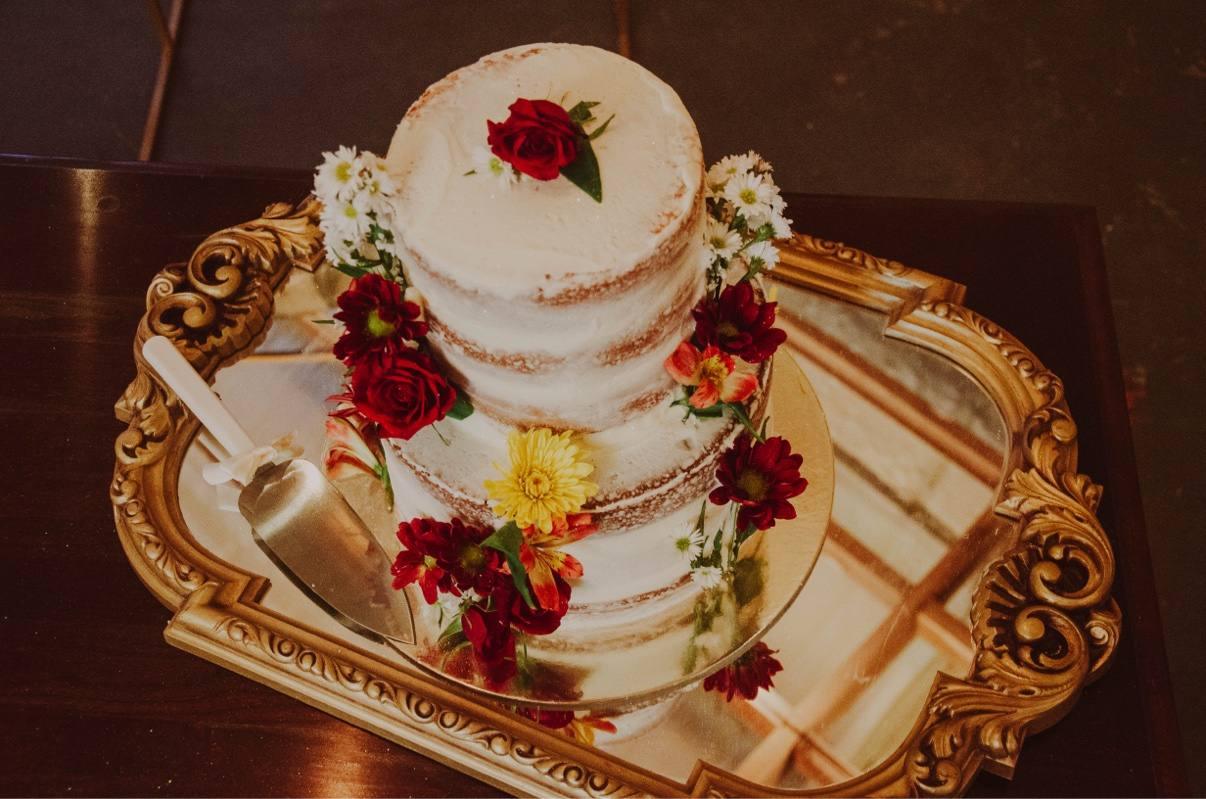 A flower-trimmed wedding cake displayed on an ornate mirrored tray