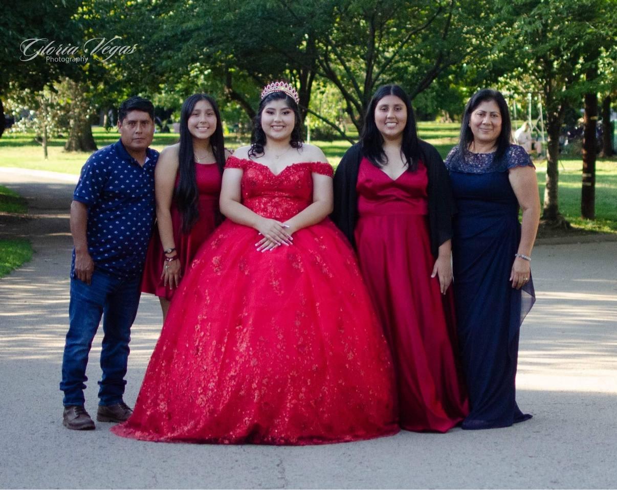 A quinceañera in a red gown and tiara posing with her family