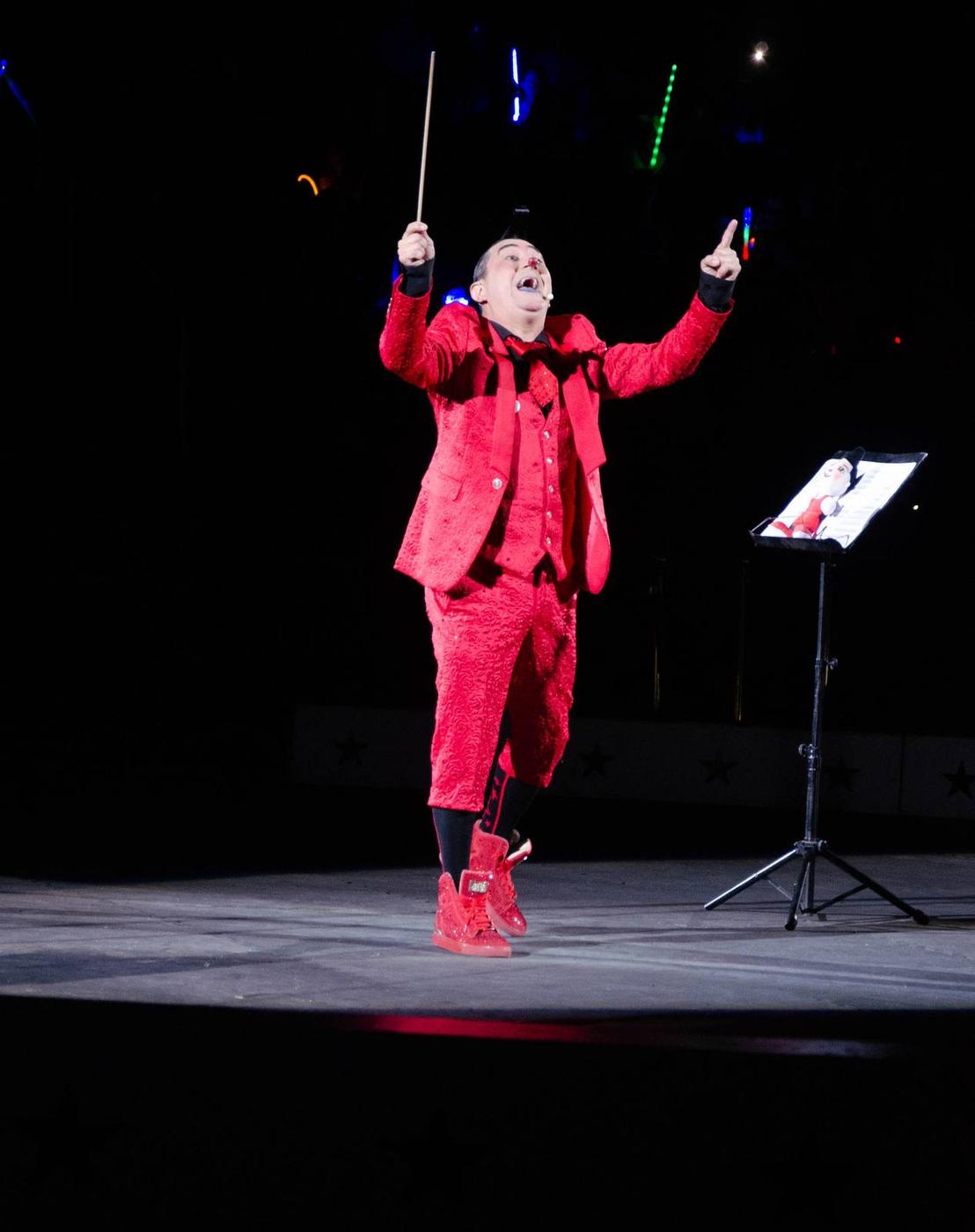A circus clown in a red suit posed under a spotlight