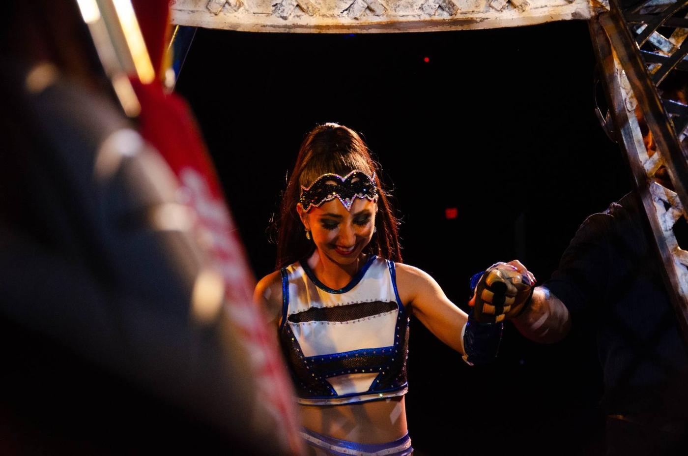 A masked circus performer illuminated in the dark ring
