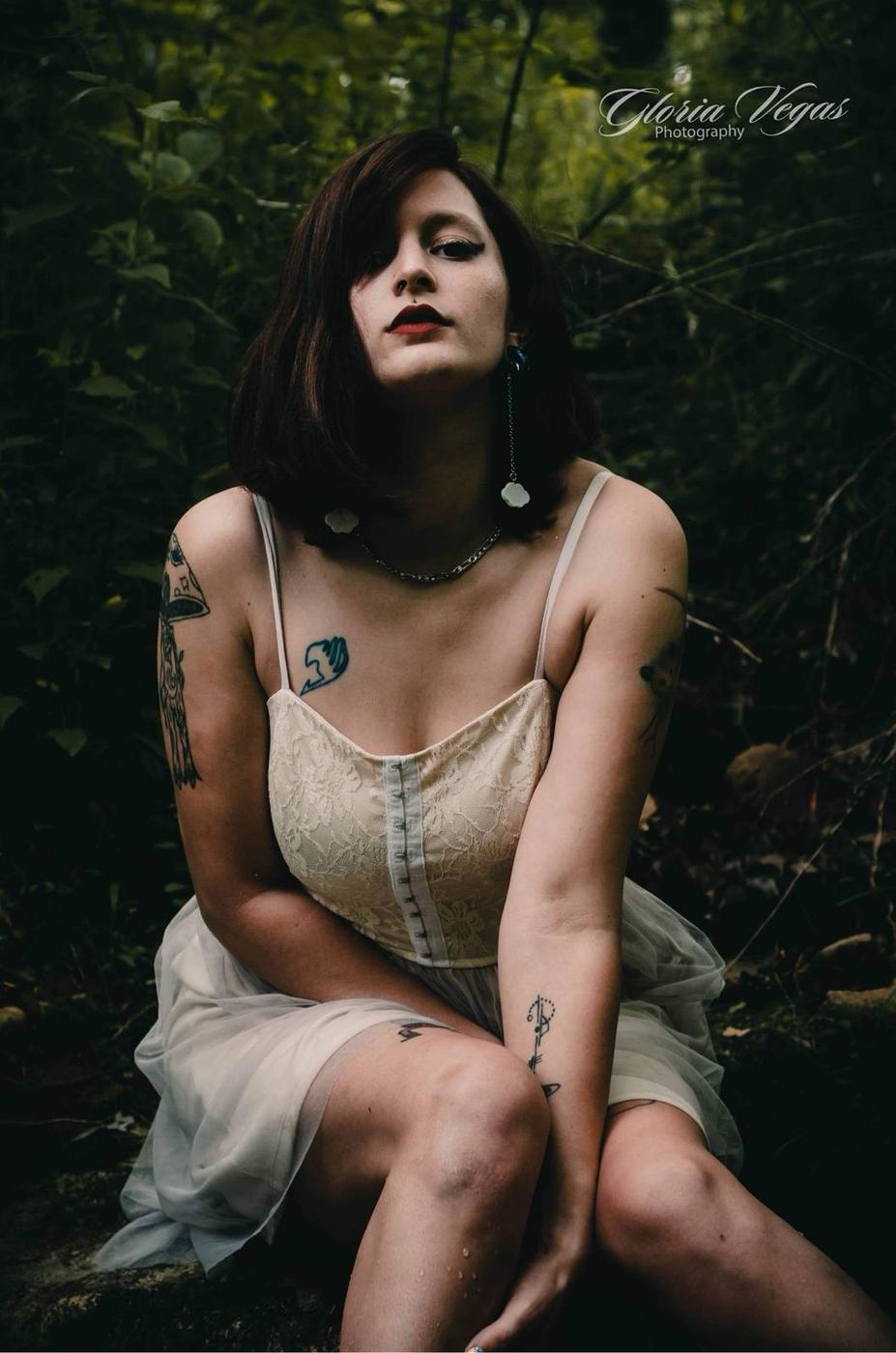 Woman in a white lace dress crouching among dark green woods