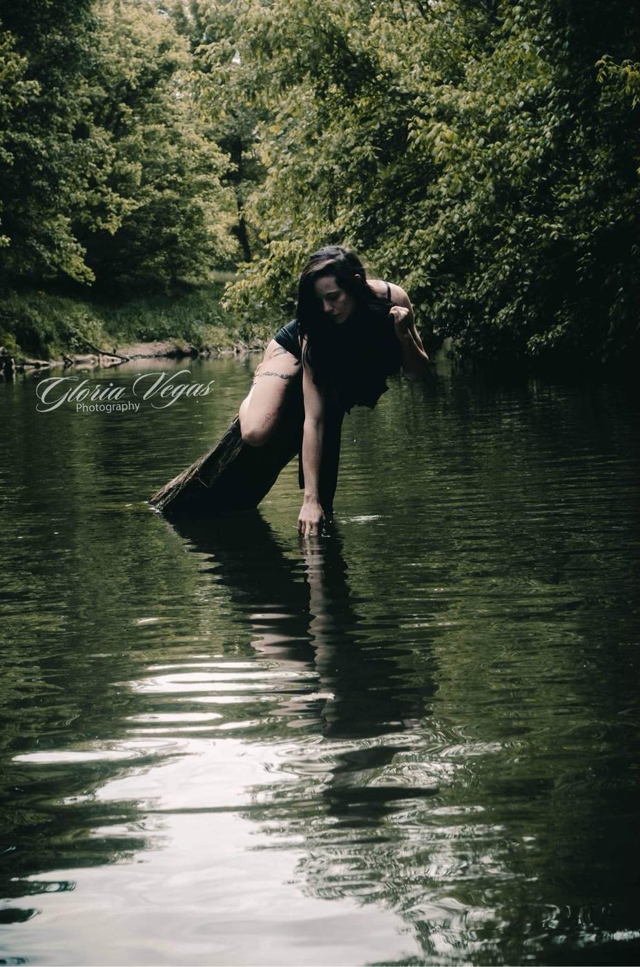 Woman standing on a fallen log in a river, trailing her hand in the water