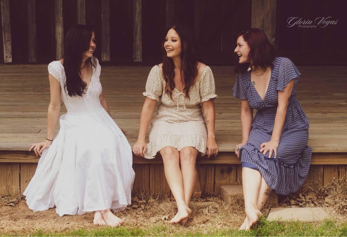 Three women laughing together while seated on a wooden porch