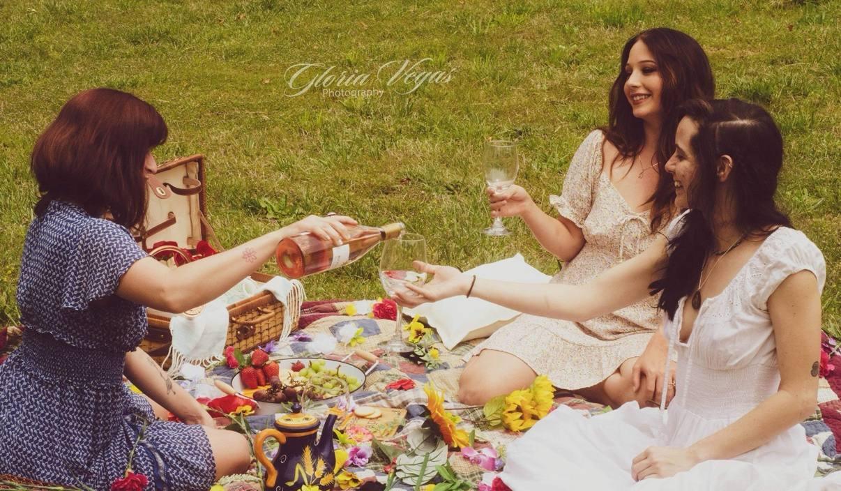 Three women sharing a bottle of wine at a cottage picnic