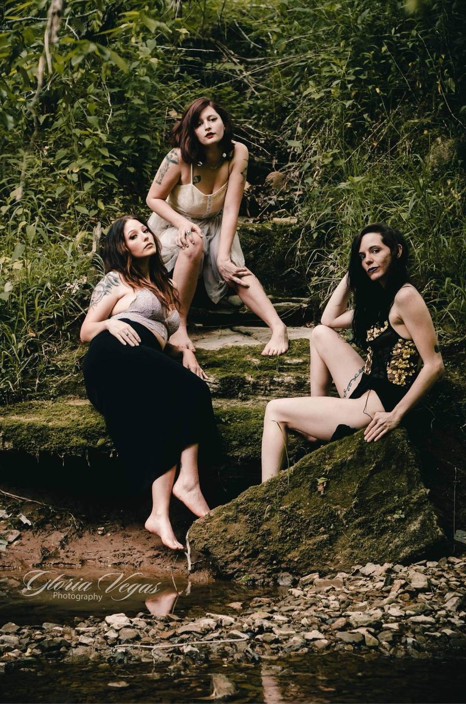 Three women posing together on mossy rocks at the edge of a creek